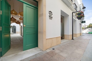 L’entrée d’un hôtel, avec une porte verte, une enseigne indiquant « Casa Pela Vega Suites » et des jardinières suspendues remplies de fleurs.