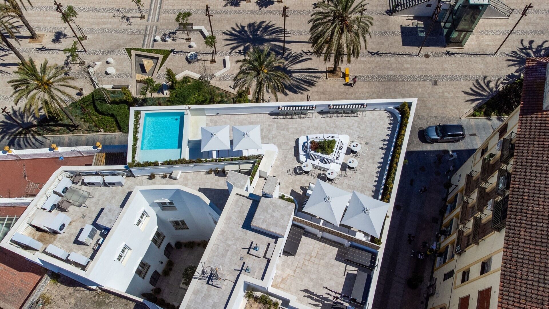 Luchtbeeld van een hotel met een zwembad op het dak, terras en palmbomen.