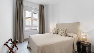 Een slaapkamer met een bed, een nachtkastje met een lamp, een raam met gordijnen en een houten bankje.