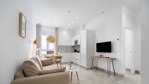 Un salon moderne avec un canapé, un coin repas avec des chaises, une cuisine équipée d’un four à micro-ondes et un téléviseur fixé au mur.