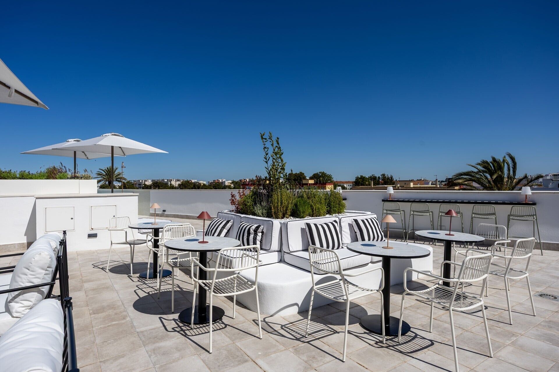 Een terras op het dak met buitenmeubilair, inclusief tafels en stoelen, en een uitzicht over de stad.