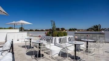Een terras op het dak met buitenmeubilair, inclusief tafels en stoelen, en een uitzicht over de stad.