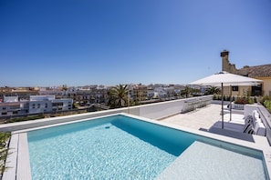 Une piscine sur le toit, avec une eau d’un bleu limpide, entourée d’immeubles et surplombant un ciel dégagé.