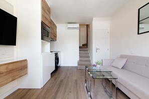 A modern kitchen with a microwave, oven, and washing machine, a glass coffee table, a sofa, and a staircase leading to a second floor.