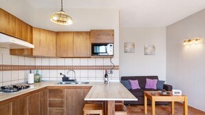 Una cocina con armarios de madera, microondas, pileta, mesa de comedor y taburete de bar.