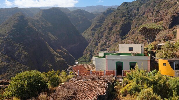 Paisaje montañoso con un edificio que presenta un techo verde y un techo de tejas rojas.
