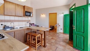 Una cocina con armarios de madera, un microondas, una zona de comedor con taburetes y una puerta verde.