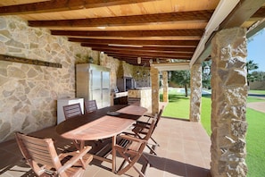 An outdoor patio with a stone wall, wooden ceiling, and a dining table with chairs.