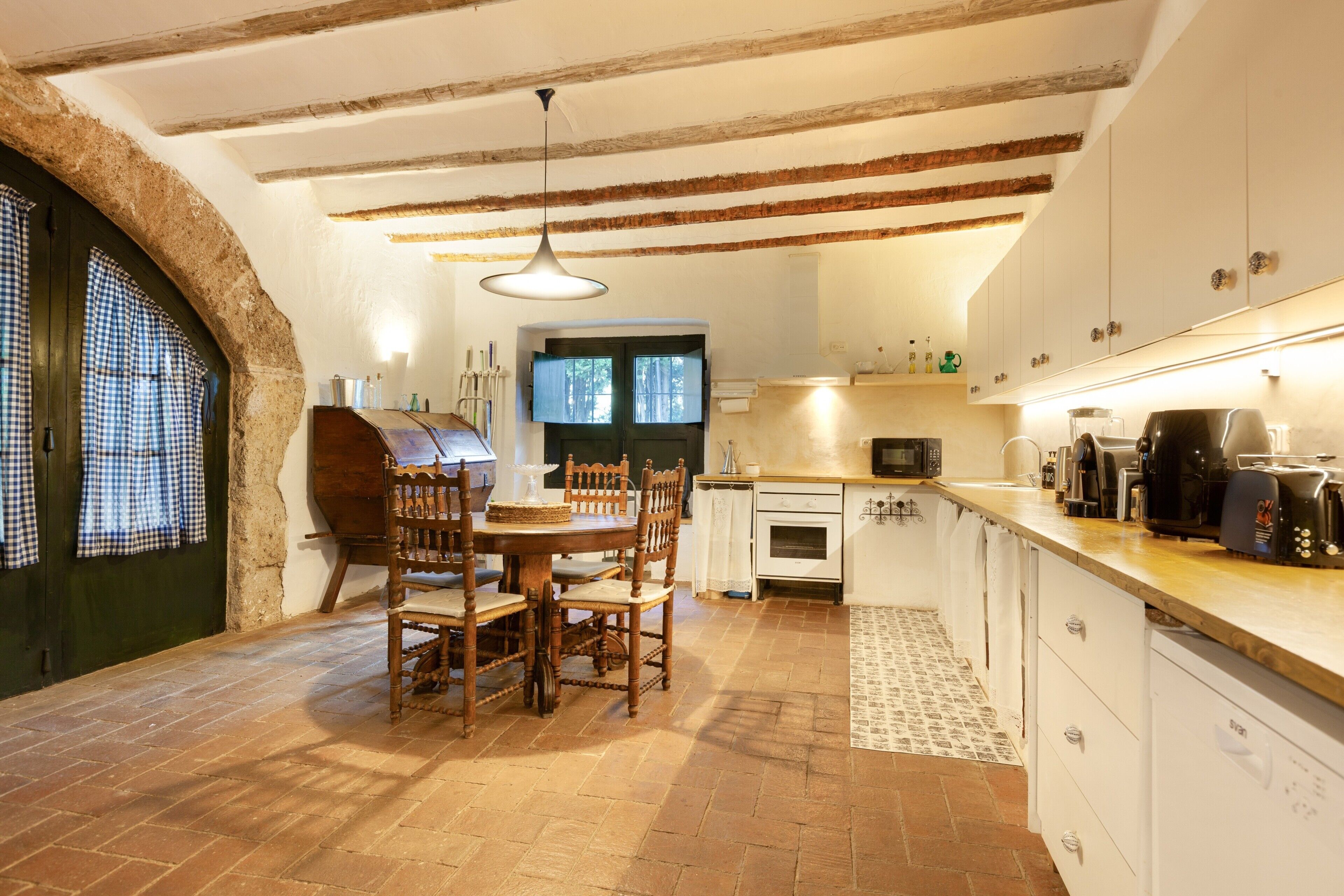 A kitchen with a dining table, chairs, a hanging light fixture, a microwave, and a coffee machine.