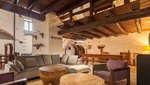 A rustic interior with exposed wooden beams, a sofa, round wooden tables, and a staircase leading to an upper level.