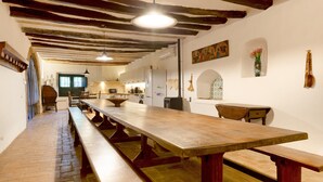 A long wooden table with benches in a rustic kitchen with exposed beams and a tiled floor.