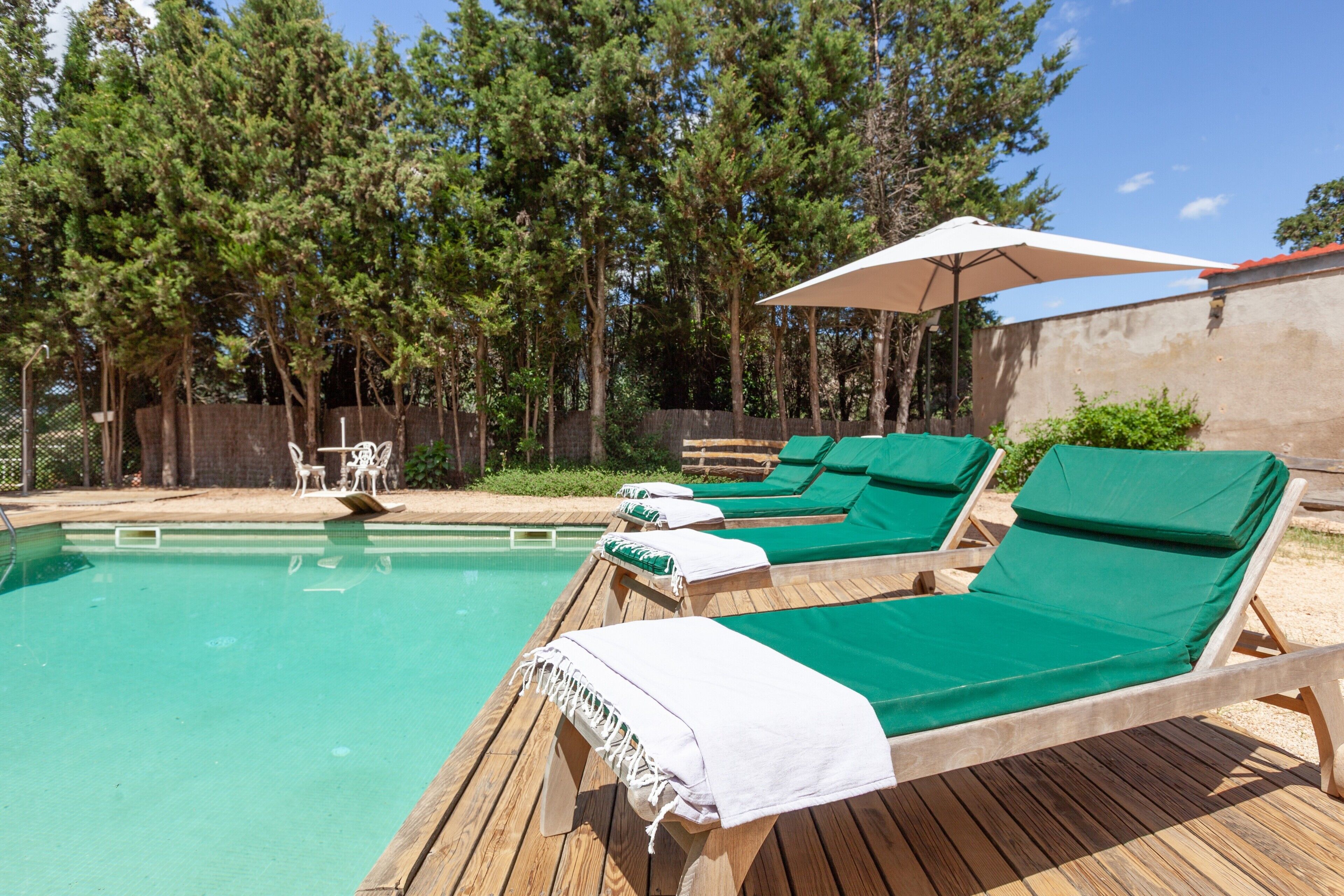 Zona de piscina con cubierta de madera, sillas de descanso y una sombrilla.