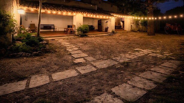 A courtyard with stone paving, a building with a tiled roof, and string lights.