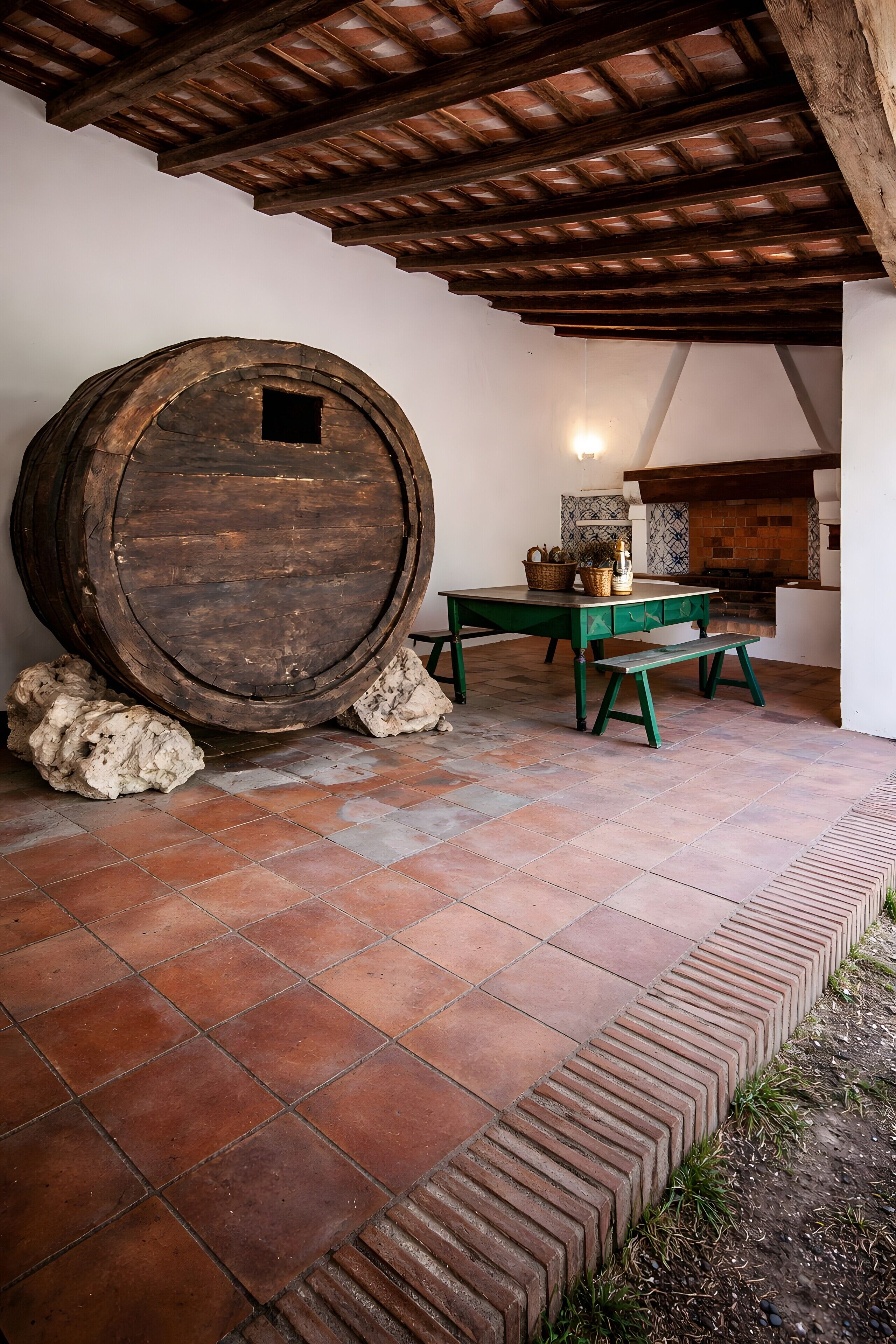 A rustic interior with a large wooden barrel, a green table, and a tiled floor.