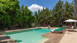 A rectangular swimming pool with a wooden deck, surrounded by trees and a wooden fence.