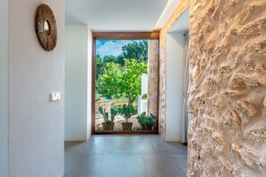 A hallway with a stone wall, a door leading to a garden with cacti, and a wall-mounted mirror. - Holiday Home 'Can Xumeu Ferrer' with Private Terrace, Wi-Fi and Air Conditioning (Formentera)