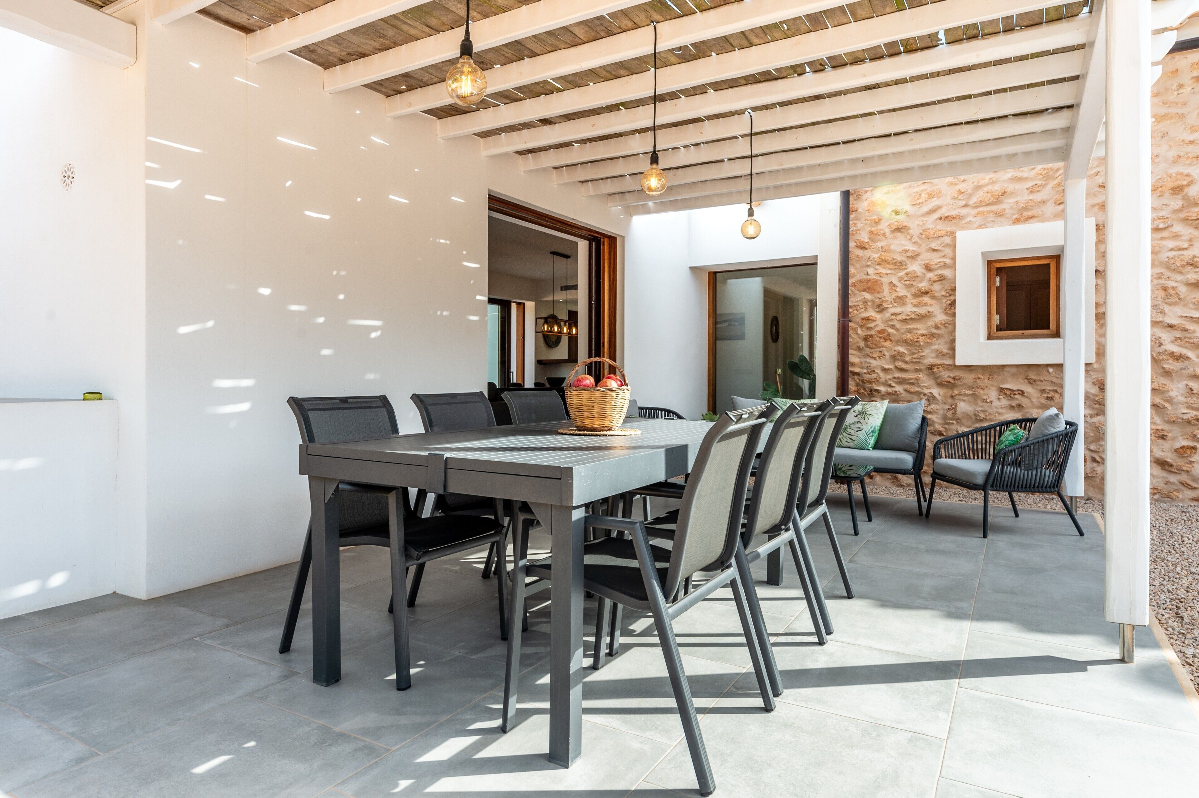 Un comedor con una mesa y sillas, una cesta de fruta y una pared de piedra.