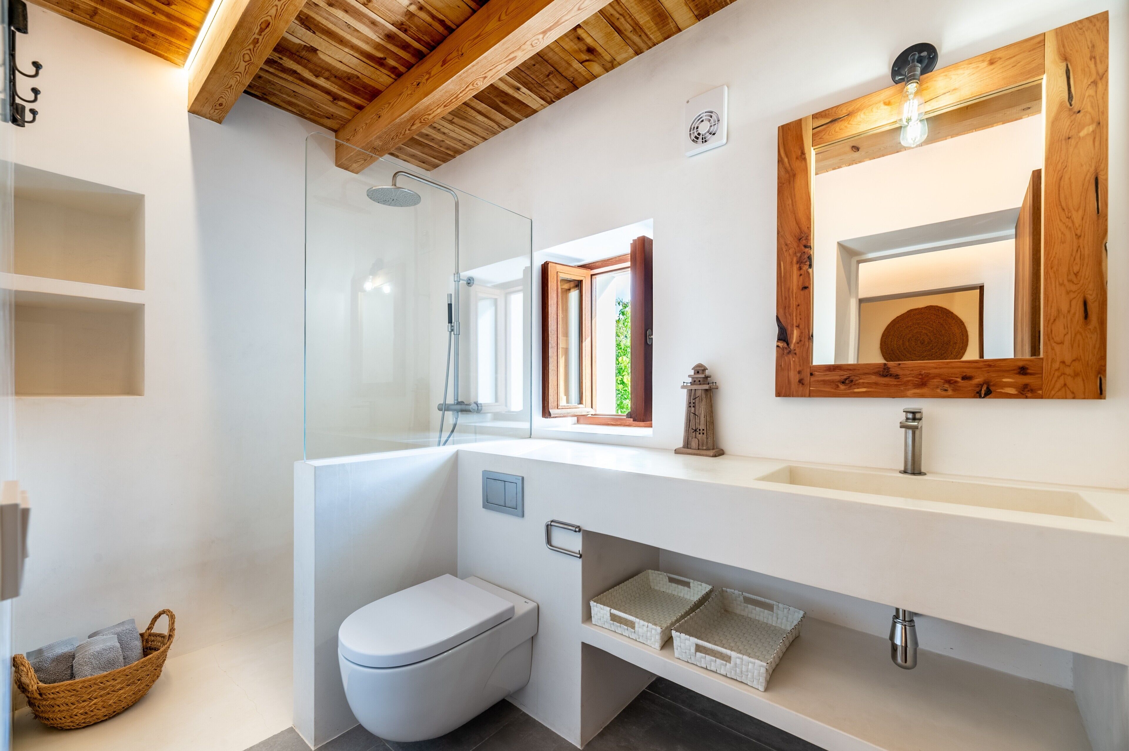 Un baño moderno con cabina de ducha de vidrio, inodoro blanco, espejo con marco de madera y lavamanos blanco sobre encimera de madera.