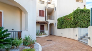Un pati amb paviment de rajoles, un edifici blanc amb balcons i un petit jardí amb diverses plantes.