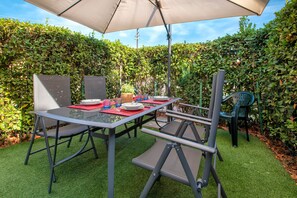 An outdoor patio with a table set for dining, surrounded by greenery and a large umbrella. - Apartment 'Gio's' with Shared Pool, Private Garden and Air Conditioning (Lu Bagnu)