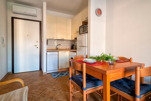 A compact kitchen with a dining area, including a wooden table, chairs, and a red placemat. - Apartment 'Gio's' with Shared Pool, Private Garden and Air Conditioning (Lu Bagnu)