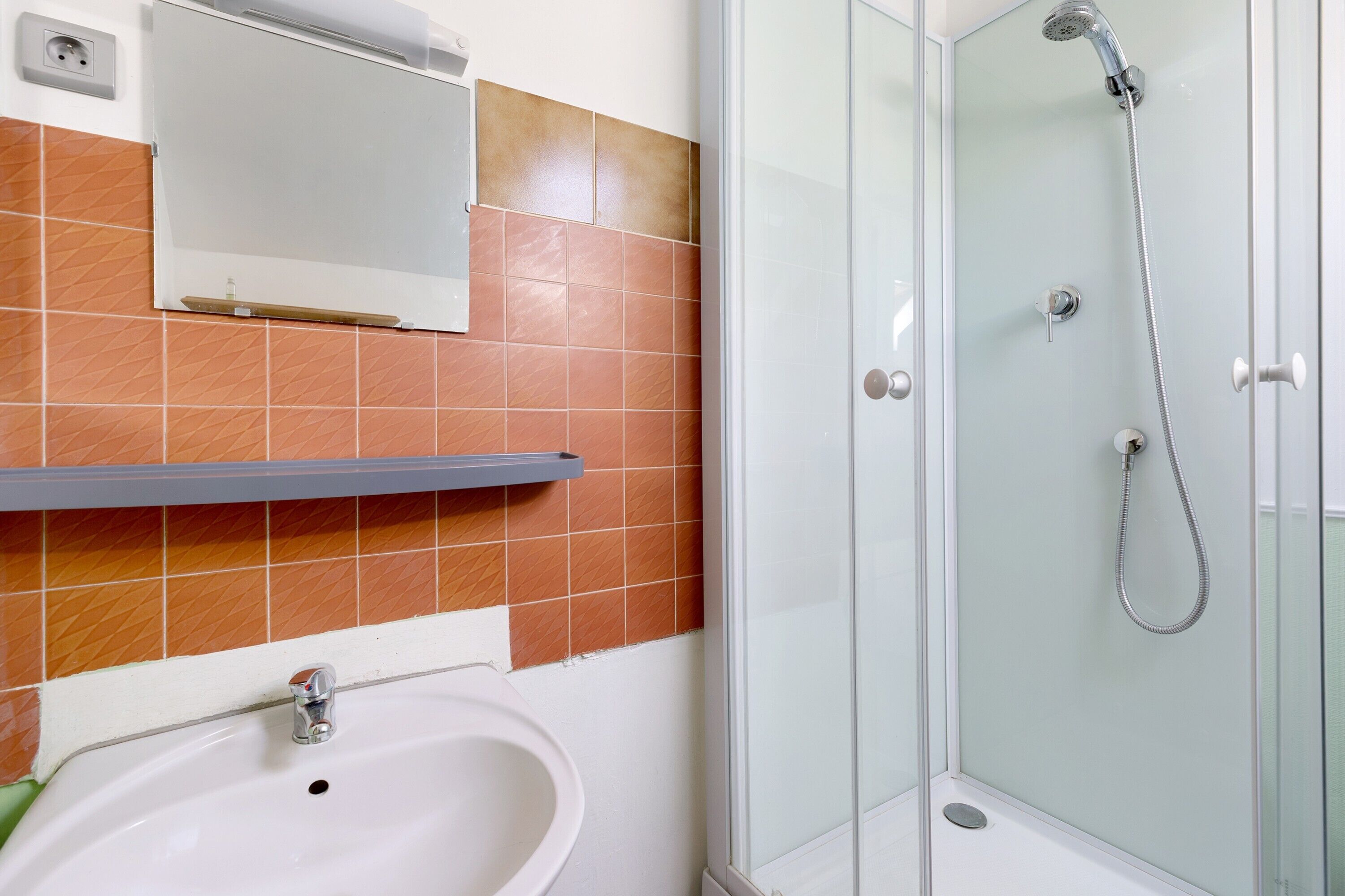 Ein Badezimmer mit Waschbecken, Spiegel, Dusche und Fliesenwänden.