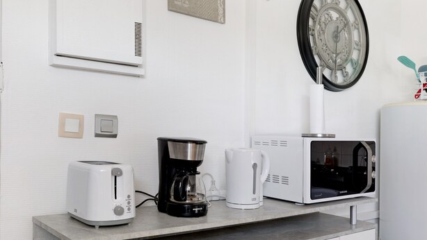 Una cocina con tostadora, cafetera, microondas y calentador de agua en la encimera.