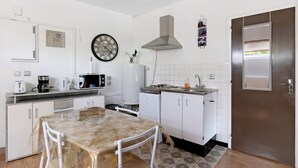 Cocina compacta con alacenas blancas, una mesa de comedor, un reloj y un microondas.