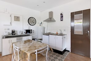 Cozinha compacta com armários brancos, uma mesa de jantar, um relógio e um micro-ondas.