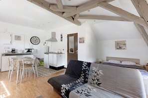 Quarto com cama, sofá, mesa de jantar com cadeiras, cozinha e um relógio na parede.
