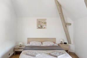Een slaapkamer met een houten hoofdeinde, een bed met beddengoed met een patroon, twee nachtkastjes met lampen en een kunstwerk aan de muur.
