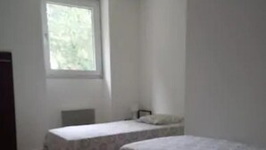 Una habitación con dos camas individuales, una ventana y una silla.