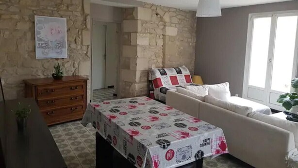 Una sala de estar con sofá, una mesa con mantel, cómoda de madera, pared de piedra y una puerta.