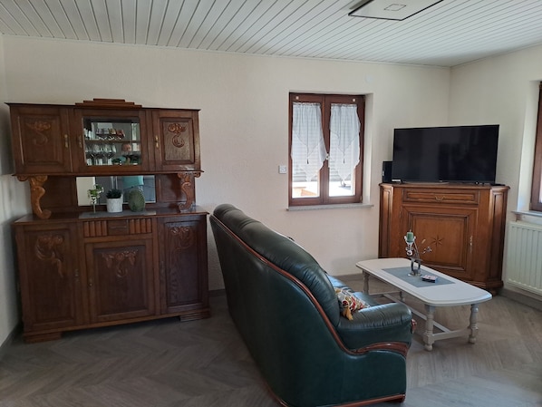 Una sala de estar con un sofá de cuero, armarios de madera, un televisor y una ventana con cortinas.