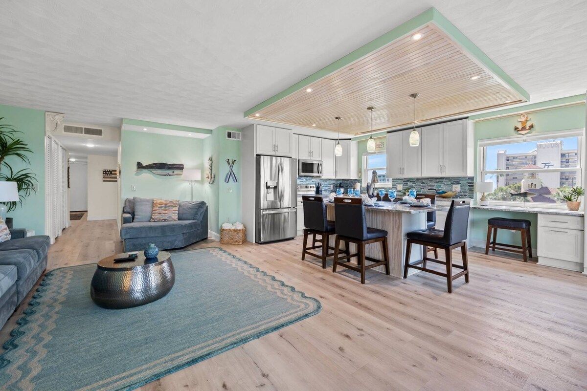 A modern kitchen with white cabinets, stainless steel appliances, and a bar area.