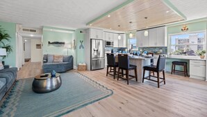 A modern kitchen with white cabinets, a stainless steel refrigerator, and a dining area with bar stools. - Updated Corner Unit! Views of the Gulf and Intercoastal! FREE Activities Included! ~ 401 Bayshores (Indian Shores)