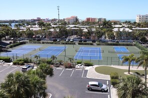 A tennis court complex with multiple courts, parking areas, and surrounding palm trees.