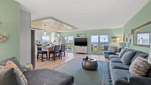 A spacious living area with a grey sofa set, a coffee table, and a TV. There is a balcony with a view of the city. - Updated Corner Unit! Views of the Gulf and Intercoastal! FREE Activities Included! ~ 401 Bayshores (Indian Shores)