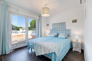 A bedroom with a bed, a nightstand, a lamp, a window with curtains, and a view of the outside.