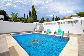 A rectangular swimming pool with clear blue water, surrounded by a white wall and a tiled deck.