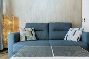 Un salon moderne avec un canapé gris, des coussins à motifs, une table d’appoint en osier et une table basse à texture intéressante.