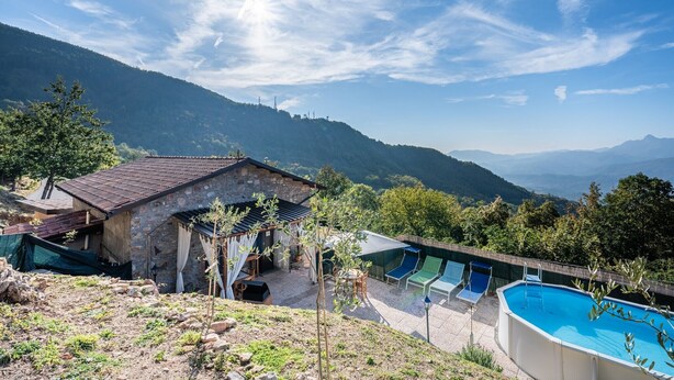 Un edificio de piedra con piscina, mobiliario exterior y vistas a las montañas.