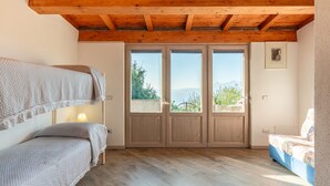 Una habitación con una cama litera, un sofá, techo de madera y una puerta que da a un espacio exterior con vistas a árboles y montañas.