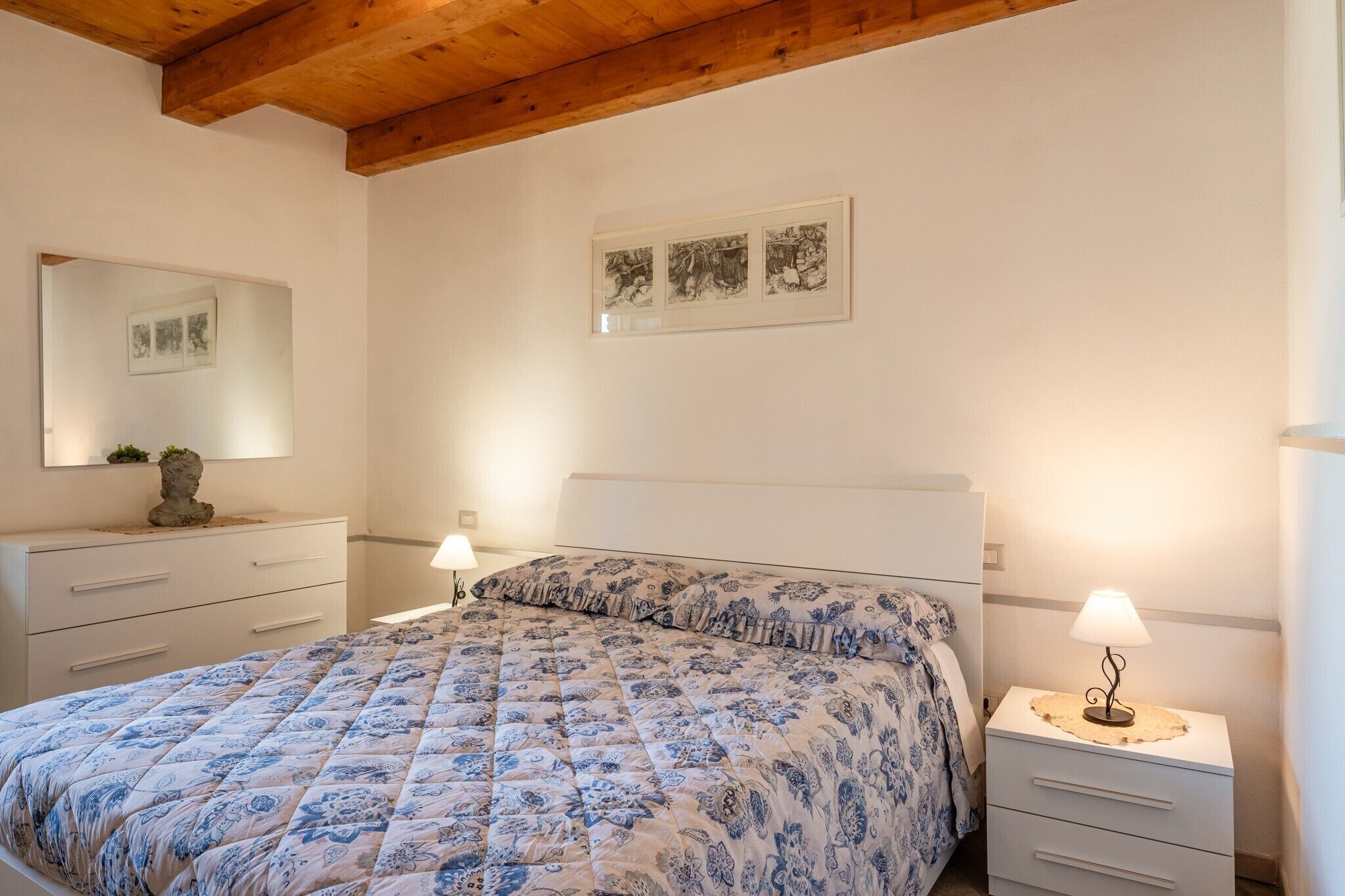 Une chambre à coucher avec un lit, des tables de chevet, un miroir et des œuvres d’art accrochées au mur.
