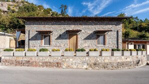 Un edificio de piedra con tres ventanas, una puerta y un pequeño porche adornado con plantas en macetas.