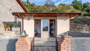 Un edificio de piedra con un porche de madera con pérgola, un pequeño porche cerrado y un muro de piedra.