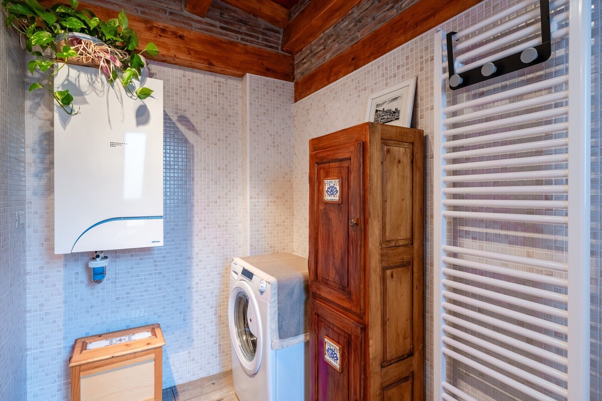 A laundry room with a washing machine, a wooden cabinet, and a tiled wall.