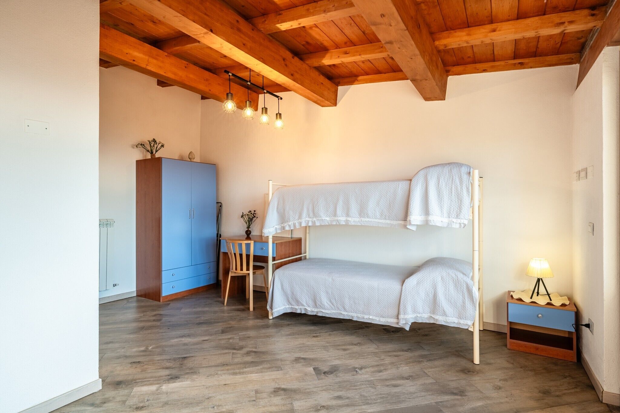 A bunk bed with a desk and chair, a wardrobe, and a nightstand with a lamp.