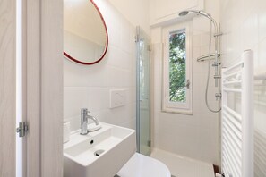 Un baño moderno con un lavabo blanco, cabina de ducha de vidrio y ventana.