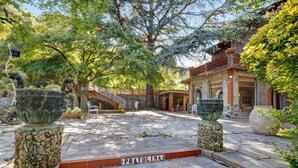 Une cour avec un sol en pierre, une enseigne indiquant « PRATOLINA », et de grands jardinières.